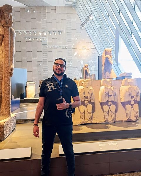 Michael Sabry next to a standing king statue in a gallery of the Grand Egyptian Museum