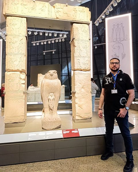 Michael Sabry beside a Horus falcon statue and an inscribed stone gateway
